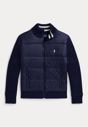 Tmavomodrá bunda na zips s prešitým predným dielom, rebrovanými pletenými rukávmi a golierom, bielo pruhovaným vnútorným golierom a malým bielym logom koňa na hrudi.