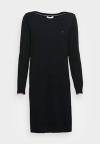 Svart stickad klänning med långa ärmar, båtformad halsringning och röda och vita randiga detaljer vid muddarna. Enkel, rak silhuett.