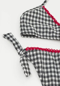 Haut de bikini en vichy noir et blanc avec une bordure en dentelle rouge, doté de bretelles réglables et d'une fermeture à nouer. Texture de tissu douce.
