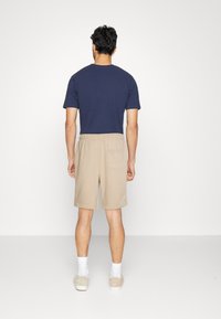 T-shirt en coton marine à manches courtes associé à un short beige à taille élastique avec une poche au dos. Le modèle est de dos.