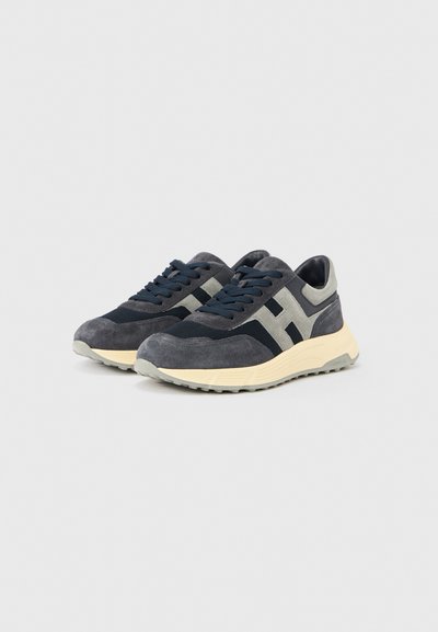 Ζευγάρι σκοτεινών γκρι και μαύρων δερμάτινων αθλητικών παπουτσιών με γκρι κορδόνια και μπεζ σόλες σε ανοιχτό γκρι φόντο.