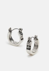 Brincos em argola prateados com uma superfície texturizada e um design ousado e robusto, apresentando um fecho e mecanismo de dobradiça visíveis.