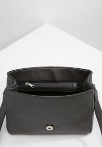 Borsa a tracolla in pelle nera con texture liscia, chiusura a scatto magnetico e scomparto interno con zip.