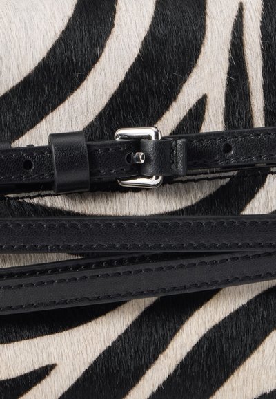 Ceinture en cuir noir avec boucle argentée reposant sur une surface en fourrure à motif zèbre montrant des rayures noires et blanches.