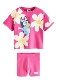 Maglietta di cotone rosa con maniche corte, caratterizzata da un personaggio e grandi fiori bianchi. Include pantaloncini rosa coordinati con un'etichetta logo blu.