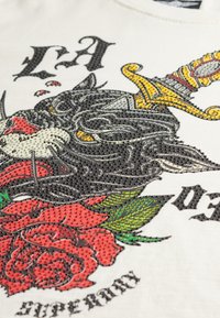 Wit T-shirt met een zwarte kat met een zwaard, versierd met strass-steentjes. Inclusief rode rozen en groene bladeren, met gedetailleerde grafische tekst.