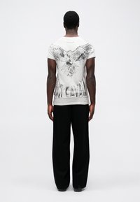 T-shirt gráfica branca com um design de águia preta e o texto "Just Cavalli" nas costas. Combinada com calças pretas largas.