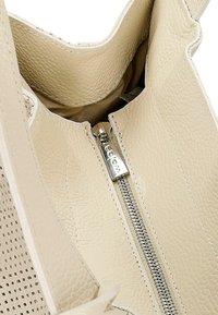 Beżowa torba skórzana w środku o teksturowanym wykończeniu, z metalowym suwakiem w kolorze srebrnym i kremowym podszewką. Projekt typu open-top bez widocznych dodatkowych elementów.