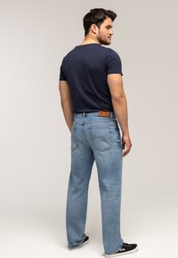 Jasnoniebieskie dżinsy z denimu o prostym kroju nogawki, z tylnymi kieszeniami, kontrastującymi przeszyciami oraz beżową skórzaną metką w pasie.