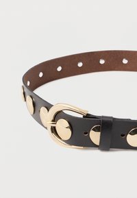 Melnas ādas josta ar zeltainiem apaļiem studiem, zelta sprādzi un gludu apdari. Iekļauj vienmērīgi izvietotas caurumiņu regulēšanai.