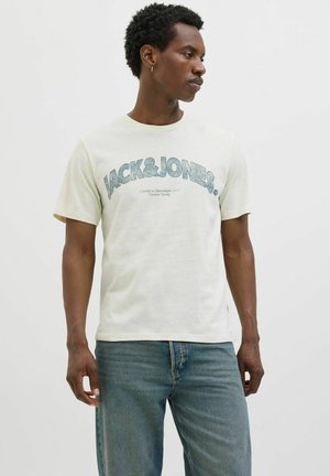 Světlý béžový tričko s nápisem "JACK & JONES" tištěným modře na hrudi. Krátké rukávy, kulatý výstřih, vyrobeno z měkké látky.