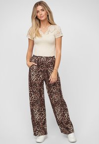 Crème kanten top met korte mouwen, gecombineerd met gestreepte bruine en beige wijde broek met een elastische tailleband en zijzakken.