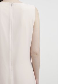 Robe rose pastel sans manches avec une silhouette droite, une texture lisse et une fermeture éclair dissimulée dans le dos.