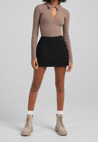 Brun randig långärmad bodysuit med nyckelhåls-krage. Svart minikjol med knappar. Beige snörkängor med vita manschetter.