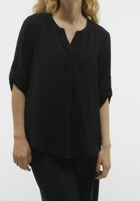 Tunic nera realizzata in tessuto texture con scollatura a V, maniche a tre quarti e una vestibilità ampia. Presenta polsini arrotolati e un design minimale.