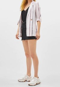 Randig blazer med beige, röd och marinblå linjer, parat med en svart linne och denimshorts. Modellen har på sig vita sportiga sneakers.