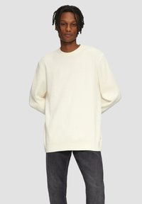 Off-white, geripptes Sweater mit rundem Ausschnitt, überschnittenen Schultern und entspannter Passform, kombiniert mit dunkelgrauen Jeans.
