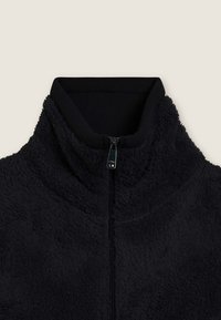 Giacca nera in pile con zip a un quarto, dotata di un colletto alto, caratterizzata da una superficie texturizzata e un bordo a coste neri a contrasto sul collo. Tirazip in metallo.