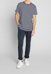 Stribet bomulds-T-shirt i navy og hvid, kombineret med mørke bukser og hvide sneakers. Enkel design med en klassisk rund halsudskæring.