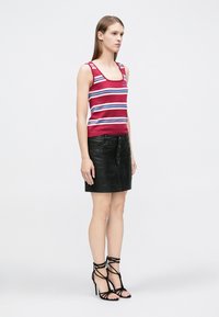 Camiseta sin mangas a rayas rojas y blancas, minifalda de cuero negra con botones al frente y sandalias negras de tacón alto con tiras.