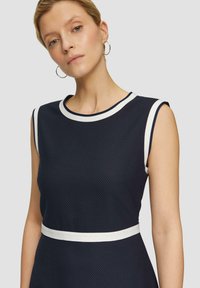 Robe navy avec un motif texturé, accents blancs au niveau du col et de la taille, sans manches et décolleté arrondi.