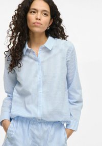 Light blue button-up shirt with vertical white and light blue stripes. Features a collar and long sleeves, made from soft fabric with a relaxed fit.