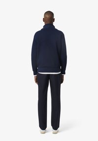 Marineblauwe fleece sweater met hoge kraag, geribbelde manchetten en zoom. Gecombineerd met bijpassende marineblauwe broek en witte sneakers. Minimalistisch ontwerp, zachte textuur.