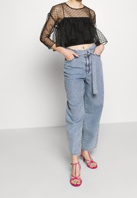 Top sheer nero con pois, maniche a sbuffo, abbinato a jeans a vita alta di un light blu e tacchi rosa con cinturini.