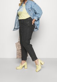Chaqueta de mezclilla, azul claro; camiseta gráfica amarilla; jeans negros; tacones amarillos de plataforma; bolsa de lona floral; atuendo casual sobre un fondo claro.