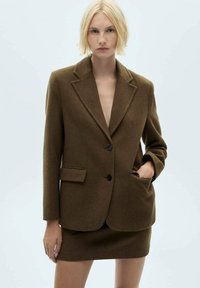 Hnedý blazer z vlnenej zmesi s klopami, dvomi prednými vreckami a jedným gombíkovým zapínaním, spárovaný s zodpovedajúcou mini sukňou.