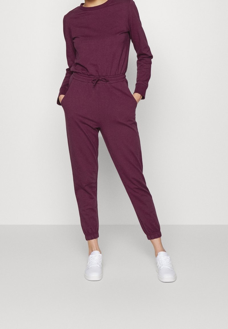 Completo jogger color marsala realizzato in tessuto morbido; maglia a maniche lunghe con scollatura tonda, vita elasticizzata e gambe affusolate; abbinato a sneakers bianche.