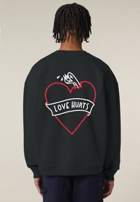 Felpa nera con vestibilità oversized, caratterizzata da una grafica a forma di cuore rosso e il testo "LOVE HURTS" in bianco, sulla schiena. Tessuto morbido.