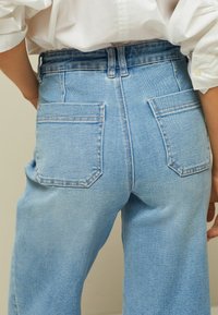 Jeans de mezclilla azul claro con corte recto, que presentan dos bolsillos traseros con detalles de costura y una cintura de altura media.