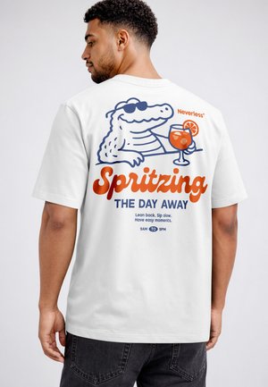 Man wearing white t-shirt with cartoon alligator holding a cocktail and text promoting relaxing between 9 AM and 9 PM.