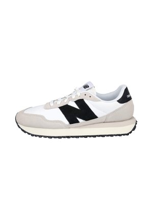 Zapatilla New Balance blanca y beige con el logo "N" en negro, cordones blancos y suela negra texturizada, mostrada de lado sobre un fondo blanco.