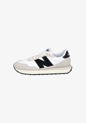 Zapatilla New Balance blanca y beige con el logo "N" en negro, cordones blancos y suela negra texturizada, mostrada de lado sobre un fondo blanco.