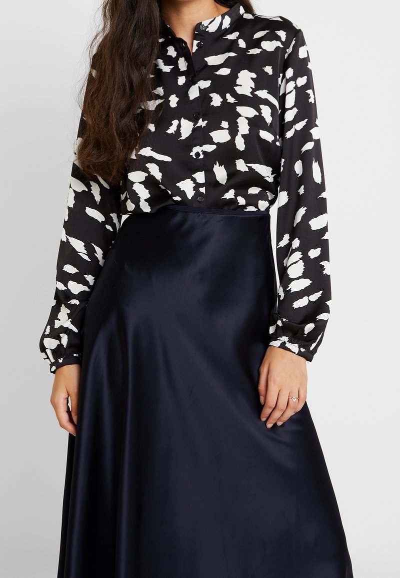 Blouse noire avec un motif abstrait blanc, boutonnée à l'avant et à manches longues, associée à une jupe en satin bleu marine lisse.