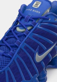 Baskets Nike Shox en bleu vif avec une tige en mesh et en synthétique, dotées d'accents argentés, de lacets complexes et d'un design de semelle notoire en matière d'amorti.