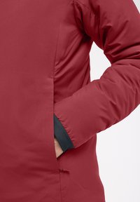 Veste isolée rouge au fini lisse, avec une manchette noire, une poche sur le côté et des détails de couture le long des coutures.