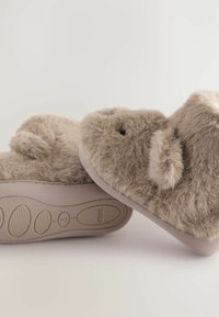 Flauschige beige Hausschuhe mit einer weichen Textur, abgerundeter Form und plüschigen Details. Gummisohle mit Grip-Muster für Halt und Stabilität.