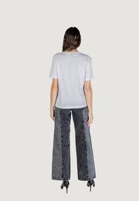 T-shirt bianco in cotone a maniche corte, abbinato a jeans in denim grigio a vita alta e a gamba larga. L'outfit è completato da tacchi neri.