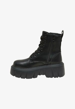 Schwarze Leder-Stiefelette mit dicker Plateausohle, ausgestattet mit einer Schnürung vorne und einem seitlichen Reißverschluss für ein einfaches An- und Ausziehen. Strukturiertes Detail entlang der Sohle.