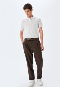 Hvid polo shirt med subtil tekstur, brune plissert bukser og hvide sneakers. Outfittet har en knaplukket krave og et læderbælte.