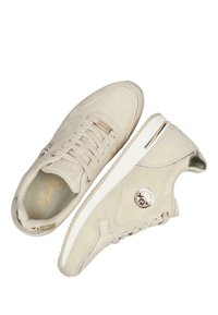 Beige plátěné tenisky s texturovaným povrchem, které mají šněrovací design, kovové akcenty a gumové podrážky. Detaily loga na boku.