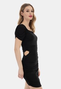 Rochie neagră dintr-un material elastic, cu pliuri, mâneci scurte tip balon, decupaje pe laterale și o siluetă ajustată.
