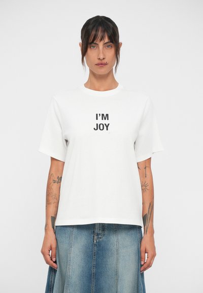 Fehér pamut póló rövid ujjú és kerek nyakkivágással. Elől középen a "I'M JOY" szöveg fekete betűkkel szerepel.