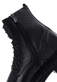Stivale alla caviglia in pelle nera con zip laterale, lace-up sul davanti, parte superiore texture e suola spessa. Gli accenti includono occhielli in metallo e cuciture.