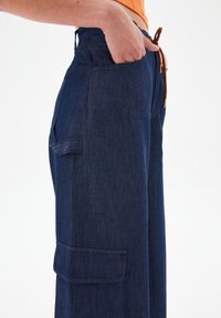 Donkerblauwe denim wijdere broek met een zijzak, een trekkoord in de taille en een zachte textuur. Heeft een casual, ontspannen silhouet.