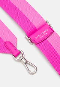 Cinghia a spalla in tessuto rosa con hardware argentato. Presenta una texture liscia e un'etichetta rettangolare con scritto "kate spade NEW YORK."