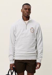 Γκρι φλις μπλούζα με ψηλό γιακά, μισό φερμουάρ και κεντημένο στρογγυλό λογότυπο στο στήθος. Ριμπ μανσέτες και τελείωμα, απαλό ύφασμα.